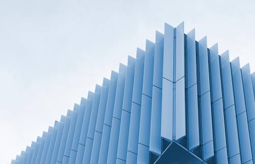 Corner of a modern building with vertical blue-tinted glass panels reflecting the sky.